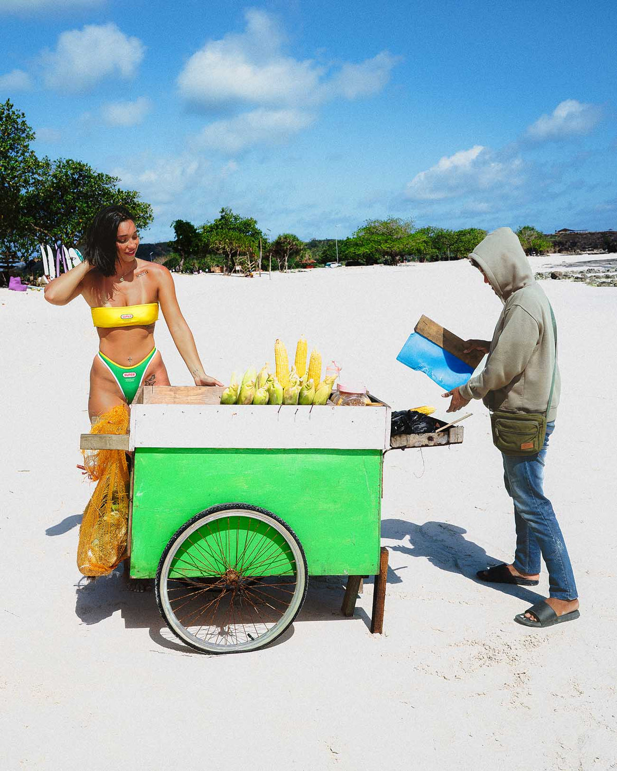 Samba Bandeau - (Thong Set) worn on the beach next to a colorful fruit cart with a vendor.