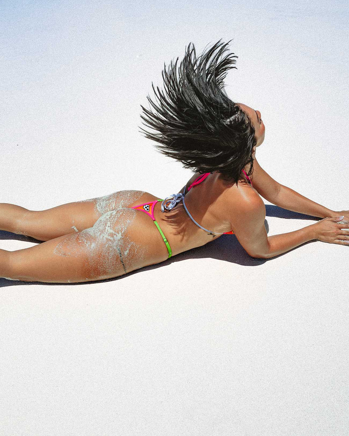 Jetski Orange - (Thong Set) worn on a model lying on the sand, showcasing the strappy triangle bikini and minimal thong cut.