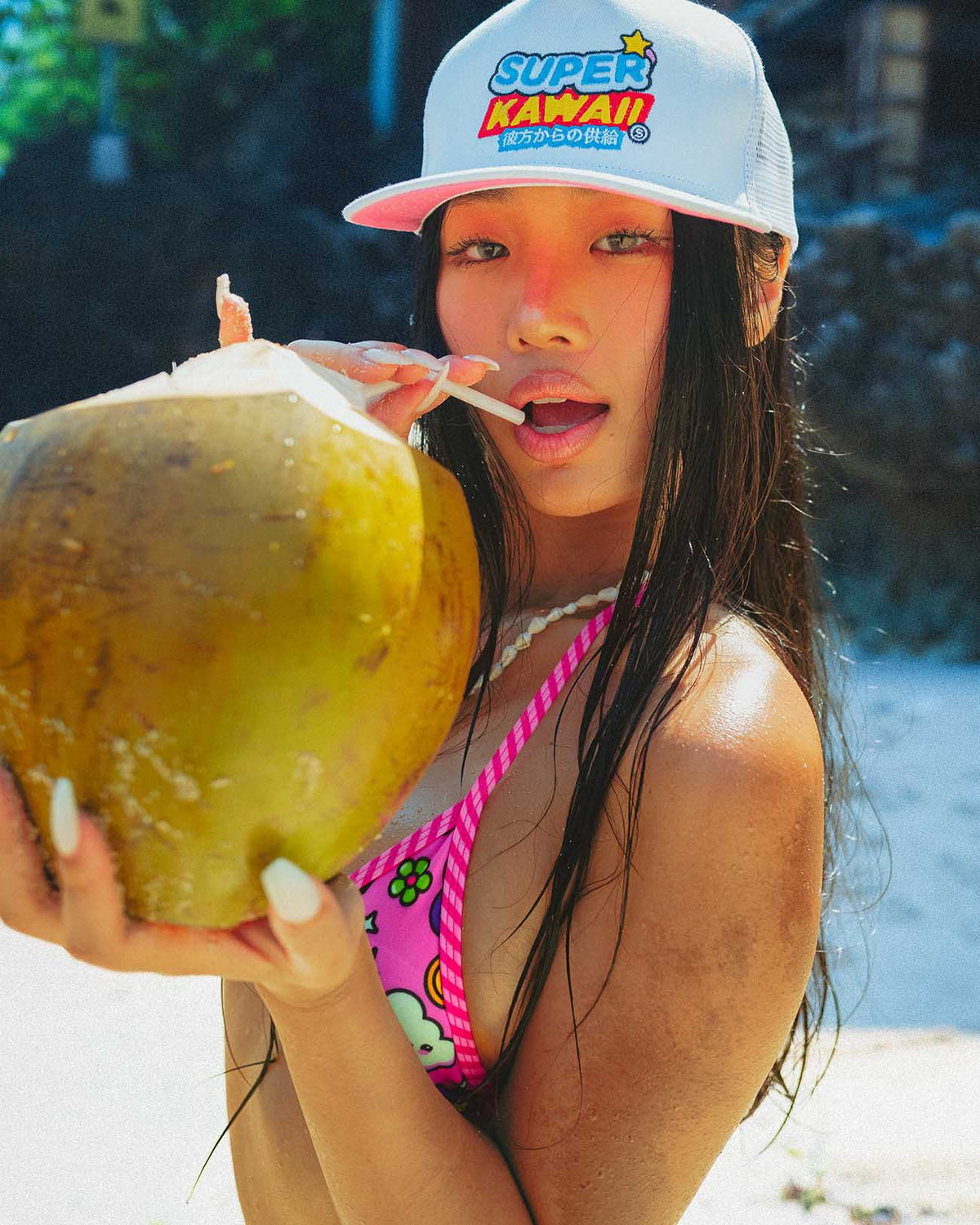 Model enjoying a coconut drink in a bright pink bikini holding a Super Kawaii cap, perfect for summer vibes.