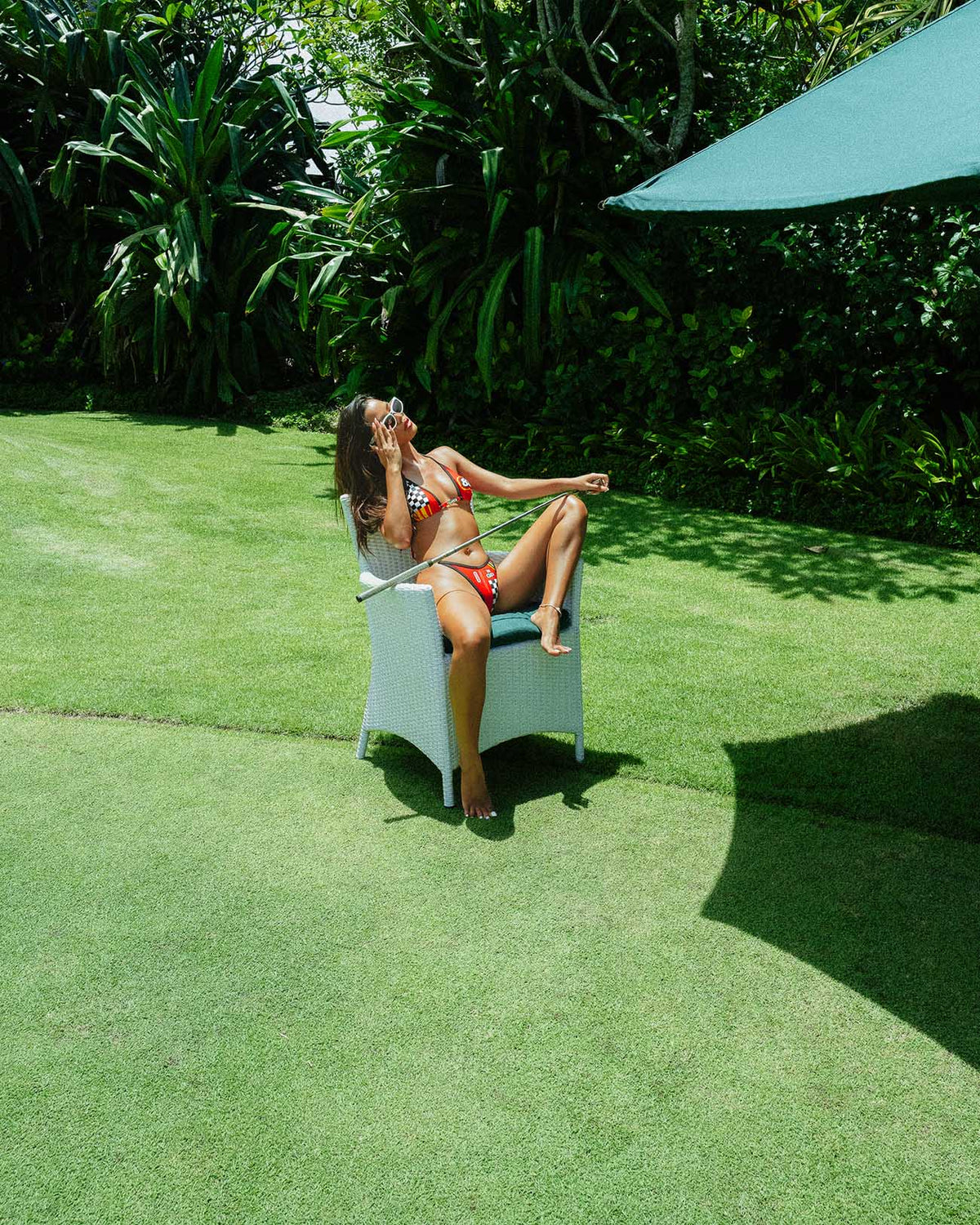 Model in Limit Red bikini relaxing on a chair in lush garden setting, showcasing sporty and vibrant swimwear style.