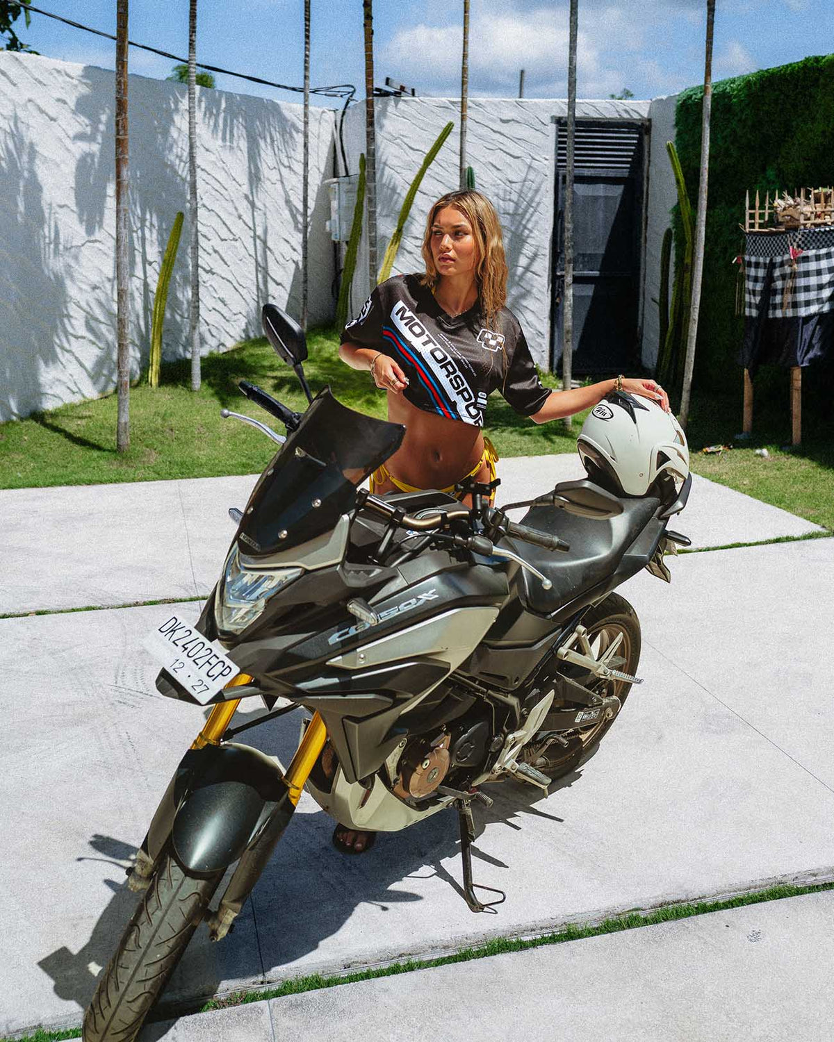 Model wearing Moto Black Jersey crop top next to a motorcycle in a vibrant outdoor setting.