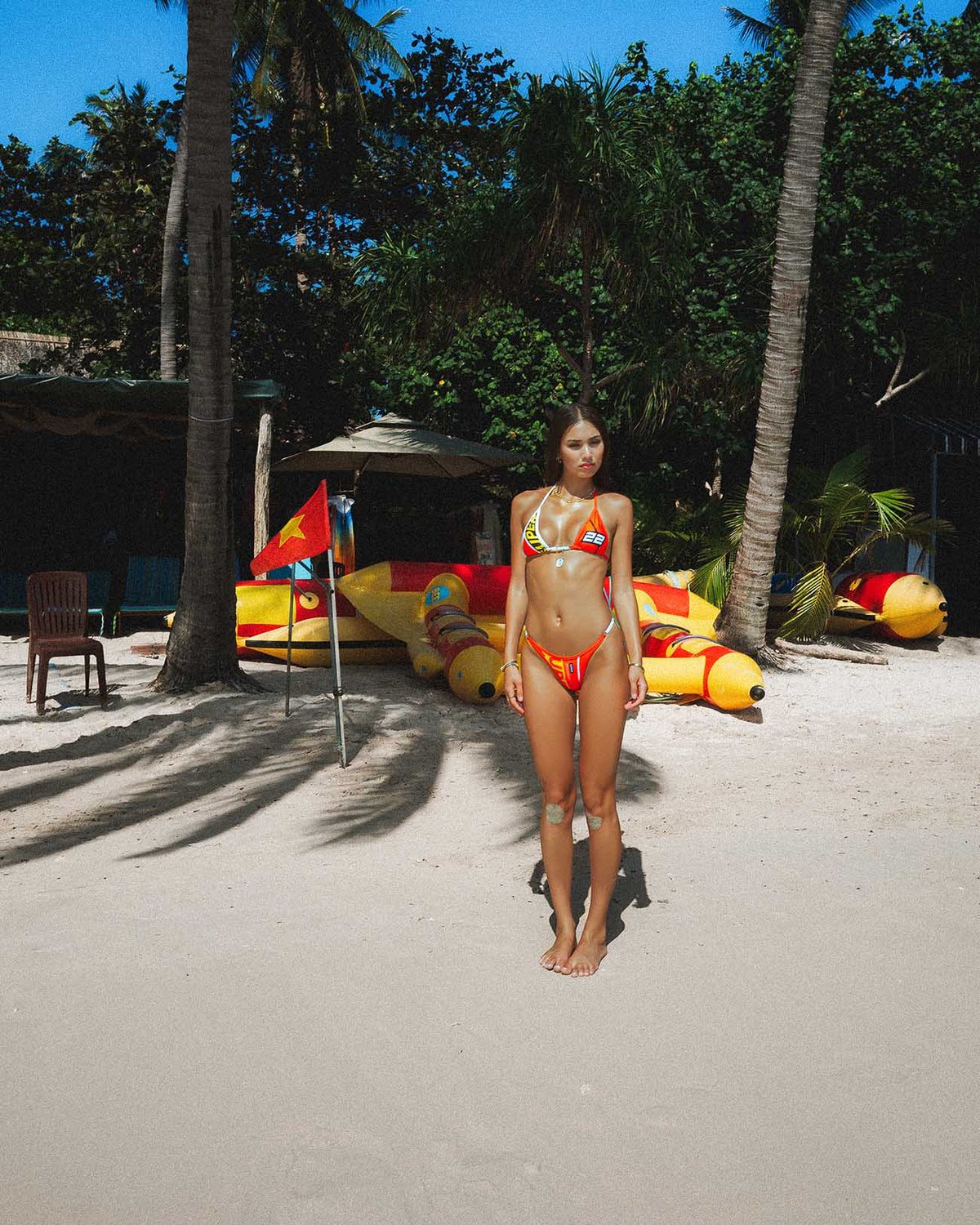 Even Faster Red - (Thong Set) model wearing thong bikini on beach with racing graphics and palm trees.